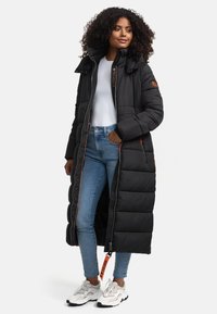 Black puffer coat with a long design, featuring a high collar, orange zippers, and side pockets, paired with light blue jeans and white sneakers.