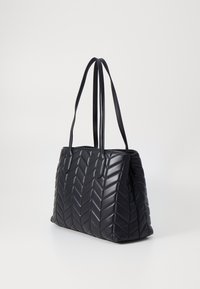Svart lær totebag med en kviltet chevron-mønster, doble håndtak og en strukturert form, med en glatt, glossy finish.