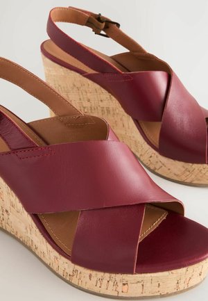 Sandalias de cuña de cuero color marrón con correas entrelazadas y plataforma de corcho. Incluyen una correa ajustable en el tobillo y suela texturizada.