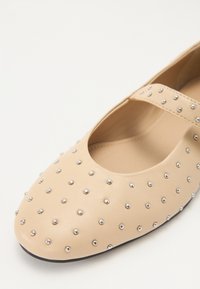 Ballerine beige in pelle liscia, con punta arrotondata e borchie decorative in argento disposte uniformemente sulla superficie.