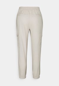 Pantalon cargo beige à taille élastique avec une coupe ajustée, comprenant deux poches latérales et une texture lisse. Convient pour une tenue décontractée.