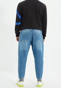 Siniset farkut, rento istuvuus, takataskuilla ja hieman haalistuneella tekstuurilla. Yhdistetty mustaan collegetakkiin, jossa on siniset raidat.