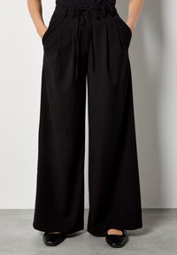 Pantaloni neri a gamba larga con vita alta, frontale plissettato e cordoncino. Presentano tasche laterali e una trama di stoffa liscia.