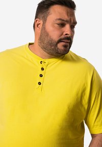 Camisa henley amarilla de manga corta con un cuello acanalado y tres botones negros en el cuello. Fabricada con un tejido suave y ligero.