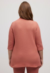 Maglione tunica pesca con un motivo testurizzato, maniche a tre quarti e orlo curvo. Materiale morbido e leggero con una vestibilità comoda.