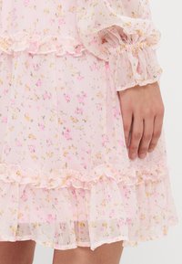 Blommig rosa klänning med volangkant och volanger vid ärmarna. Lätt och genomskinligt tyg med små gula och rosa blommor samt subtila vertikala ränder.