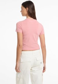 Šviesiai rožinė trumpomis rankovėmis viršutinė dalis su prigludusiu dizainu. Dėvimi su šviesiai baltais kargo džinsais, turinčiais užsegamas kišenes. Lygus paviršius, kasdienis stilius.