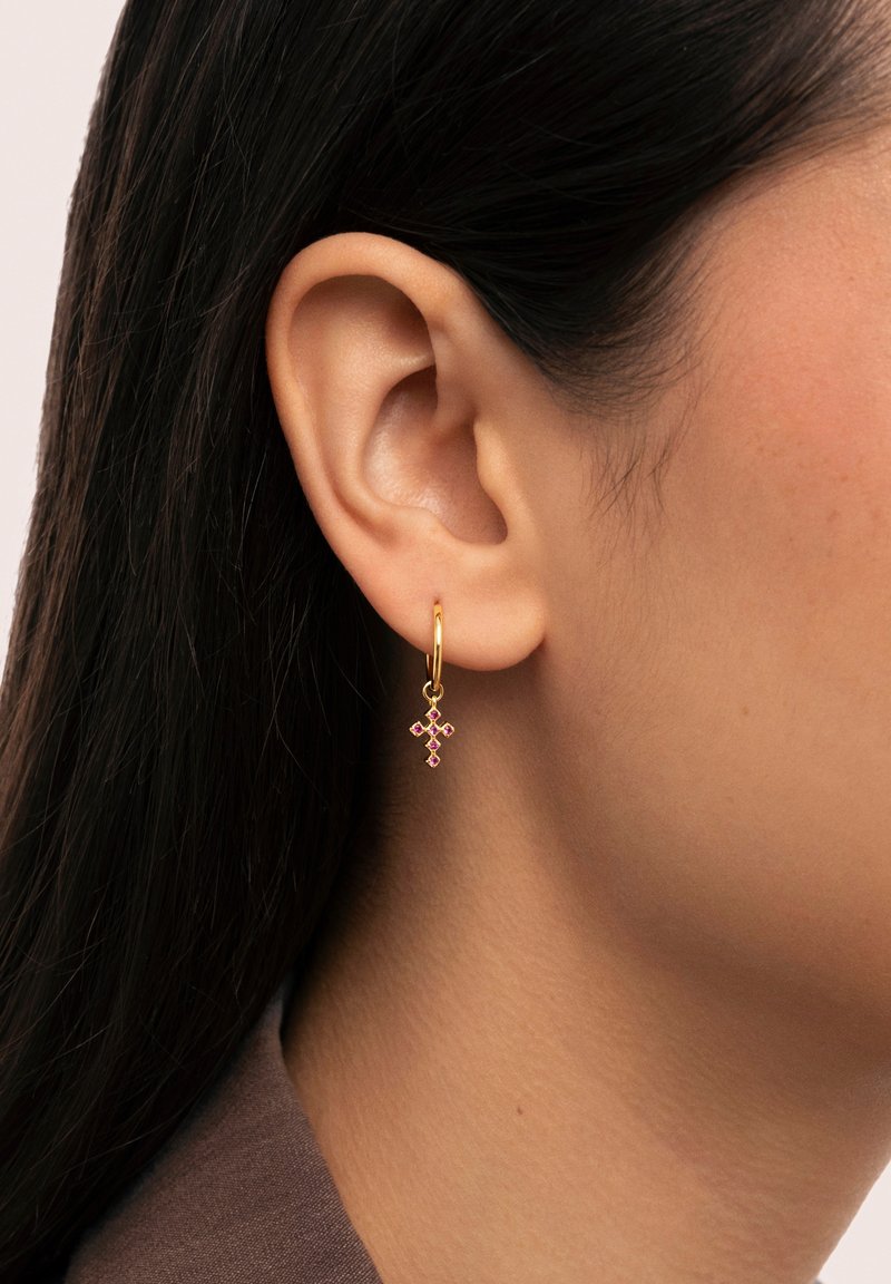 Orecchino a cerchio in oro con un pendente a forma di croce, decorato con gemme rosa. Il design è delicato e intricato, mettendo in evidenza dettagli fini.