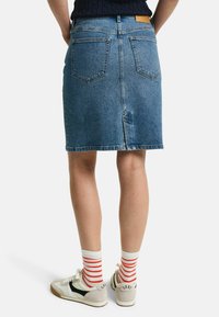 Denim rok, middelmatig lang, lichtblauw, achterzakken, gestikte zoom. Gepaard met off-white sneakers en witte sokken met rode strepen.