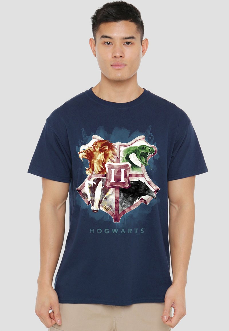 Man wearing a navy blue T-shirt with a Hogwarts crest featuring a lion, snake, badger, and eagle.