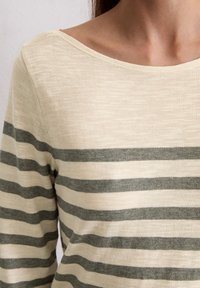 Helle beige Langarmbluse mit dunkelgrünen horizontalen Streifen. Weicher, strukturierter Stoff mit weitem Ausschnitt und lässiger Passform.