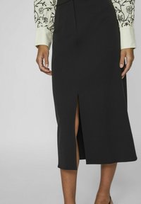 Zwarte midi-rok met een voorkeursplit, gemaakt van een gladde stof. Gedetailleerd met een slim fit taille en een nette snit, gecombineerd met een geblokte blouse.