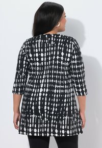 Czarna i biała tunika z odważnym, abstrakcyjnym wzorem. Posiada rękawy o długości do łokcia i luźny krój, wykonana z lekkiego materiału.