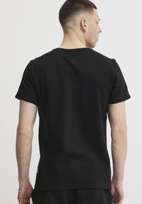 Sort kortærmet t-shirt i ribbet stof, som har en rund halsudskæring, almindelig pasform, og ses fra ryggen.