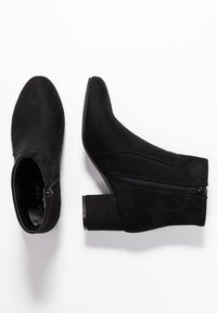 Botines de ante negros con punta afilada, cierre de cremallera lateral y tacón grueso. Textura suave, diseño minimalista y sin adornos visibles.