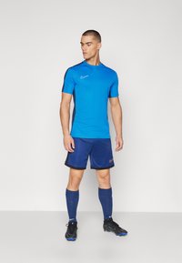 Sinine spordipusa mustade aktsentidega, koos tumesiniste lühikeste pükste, siniste sokkide ja mustade jalgpallijalanõudega. Nike logo on silmapaistvalt esitatud.