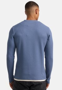 Blauw shirt met lange mouwen, gemaakt van getextureerde, geribbelde stof. Heeft een ronde hals en een strakke pasvorm, gedragen over een witte top.