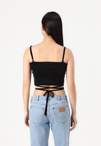 Fekete, rövidített tanktop vékony pántokkal, hátul megkötős kialakítással. Világoskék, magas derekú farmernadrággal párosítva.