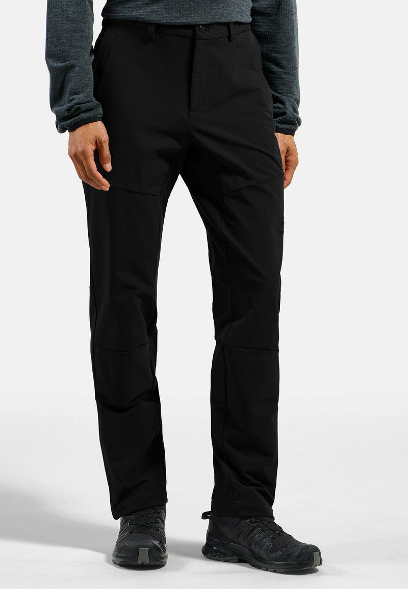 Schwarze Outdoor-Hosen mit glatter Textur, Fronttaschen und verstärkten Kniepartien, kombiniert mit schwarzen Wanderschuhen.