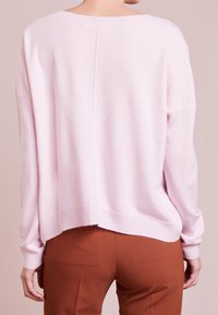 Luźny sweter w pastelowym różowym kolorze z prążkowanymi mankietami i dołem, wykonany z miękkiego materiału, z szerokim dekoltem i lekko skróconym tyłem.