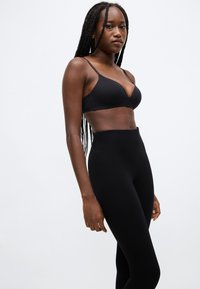 Sort bh med dyb udskæring og tynde stropper, kombineret med sort høj-taljede leggings. Glat tekstur og tætsiddende design.