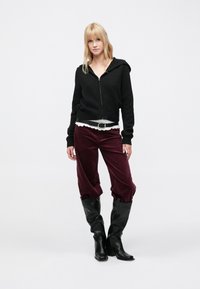 Hanorac negru cu fermoar, cămașă albă cu volane, pantaloni burgundy din catifea cu dungi, cizme negre cu toc. Design simplu, conic, cu țesătură texturată.