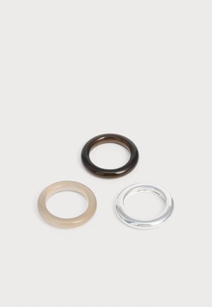 Drei glatte, kreisförmige Ringe in Schwarz, Beige und Silber auf einem schlichten weißen Hintergrund, angeordnet in einem dreieckigen Muster.