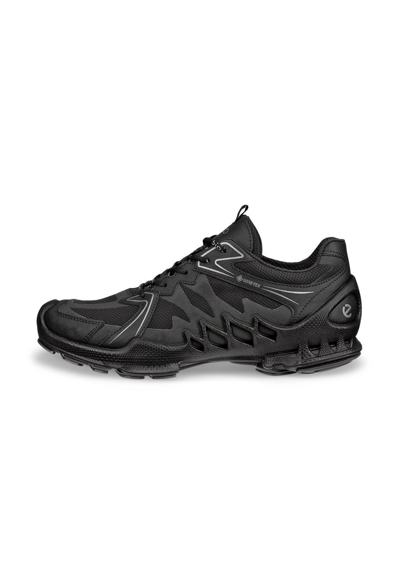 Chaussure de sport noire avec une tige en mesh et synthétique, détails texturés et semelle rembourrée. Elle possède un design à lacets et des rainures prononcées.