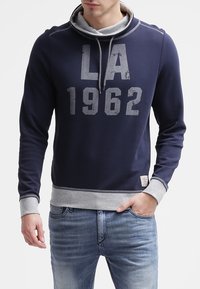 Felpa blu navy con cappuccio grigio, caratterizzata da una stampa usurata "LA 1962". Maniche e orlo a coste, realizzata in tessuto morbido.