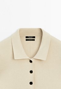 Beige knitted polo shirt with collar and three black buttons, labeled 100% cotton by Massimo Dutti.