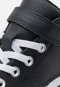 Czarne skórzane trampki z białymi sznurówkami, rzepem i srebrnymi oczkami. Tekstura jest gładka z lekko wytłoczonym wykończeniem.