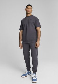 Grijze sport T-shirt en bijpassende joggers met zakken; stof lijkt zacht; blauwe en witte sneakers met bruine accenten. Zwart logo op de borst.