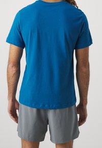 Blå bomullströja med korta ärmar, slät textur och rund halsringning, tillsammans med grå shorts gjorda av lätt material.