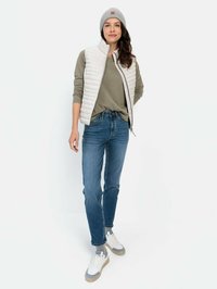 Leichtgewichtige, gesteppte Weste in Off-White, kombiniert mit einem grauen Langarmshirt, dazu blaue Jeans und weiße Sneakers mit grauen Akzenten.
