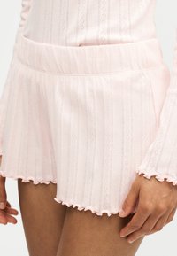 Short en maille côtelée rose clair avec une large ceinture élastique et un ourlet froncé, porté avec un top manches longues assorti.