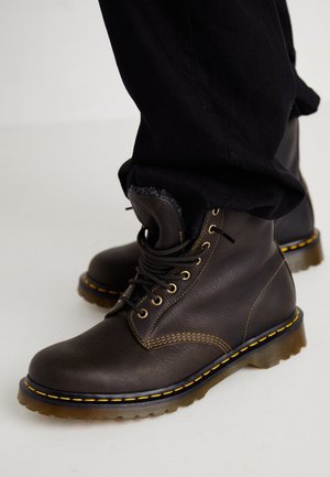 Donkerbruine leren veterlaarzen met gele stiksels en dikke rubberen zolen, gedragen met zwarte broek.