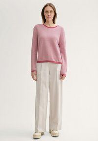 Rosa strukturierter Pullover mit langen Ärmeln und rundem Ausschnitt, kombiniert mit weißen weiten Hosen und beigen Plateauschuhen.