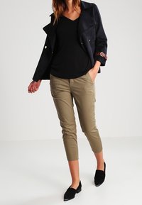 Svart t-shirt med v-ringning, mörk marinblå mockajacka med guldknappar och bruna accenter, kaki korta byxor och svarta slips-on skor.