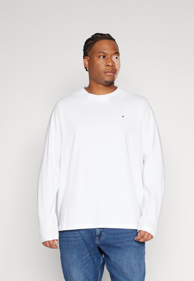 Hvit langermet t-skjorte laget av bomull, med rund hals og en liten logodetalj på brystet, paret med blå jeans.