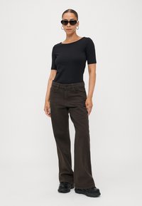Top nero a maniche corte abbinato a pantaloni larghi color marrone. L'outfit presenta una texture liscia ed è completato da occhiali da sole neri e scarpe chunky.