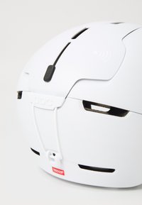 Casco bianco con fessure di ventilazione, cinturino regolabile e etichetta RECCO. Superficie liscia con un design elegante e accenti minimalisti.