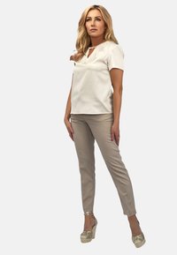 Beżowa bluzka z krótkimi rękawami i dekoltem w serek, zestawiona z dopasowanymi beżowymi spodniami i złotymi butami na koturnie. Gładki materiał z minimalnymi akcentami.