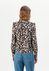 Blusa marrone e crema con motivo, maniche lunghe, dettaglio a pieghe sul retro e superficie liscia, abbinata a jeans blu a vita alta.