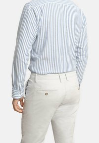 Camisa a rayas azul y blanca con puños abotonados, combinada con chinos de color claro que tienen dos bolsillos traseros y detalles de botones.