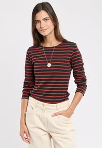 Maglietta nera a maniche lunghe con righe orizzontali rosse, vestibilità casual, indossata con pantaloni beige. Accompagnata da una collana con pendente a conchiglia.