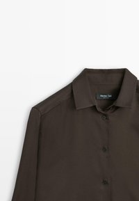 Camicia button-up marrone realizzata in tessuto liscio. Presenta un colletto classico, maniche lunghe e bottoni neri lungo la parte anteriore.