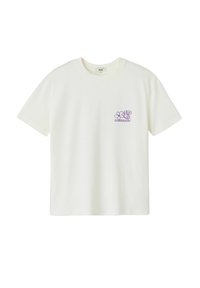 T-shirt en coton blanc avec un décolleté rond, des manches courtes et un design floral violet sur la poitrine gauche, qui comprend le texte "CHAMP de FLEURS".