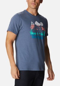 Camiseta de algodón azul para hombre con un estampado gráfico colorido de paisaje al aire libre que incluye árboles y sol, de manga corta y cuello redondo.