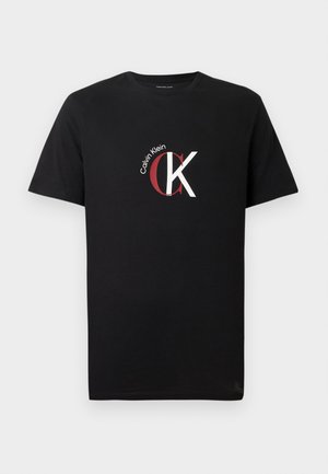 Musta puuvillainen t-paita, jossa on valkoinen ja punainen "Calvin Klein" -logo ja etuosassa tyylitelty "CK"-graafinen kuvio. Lyhyet hihat.