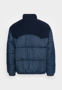Denim puffjacka med ett mörkblått kordpanel vid axlarna, ribbad mudd och en något kortare, boxig silhuett.